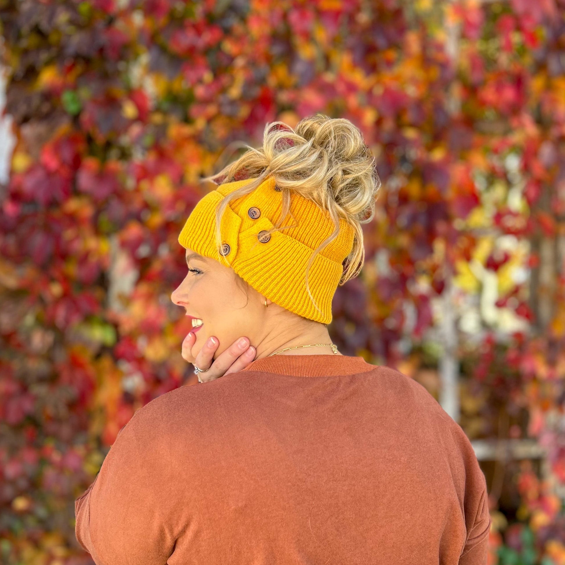 side view of women with mustard button up beanie with large messy bun out the top