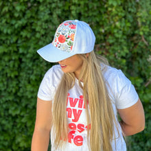 Load image into Gallery viewer, side view of girl wearing white floral hidden messy bun baseball cap with white and coral flowers
