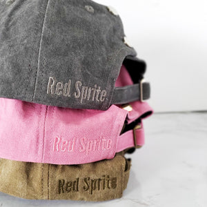 close up view of red sprite hats logo on dark grey, pink, and olive green messy bun baseball caps