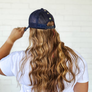 back view of dark blue mesh back messy bun baseball cap with silver snaps red sprite hats. Long curly hair 